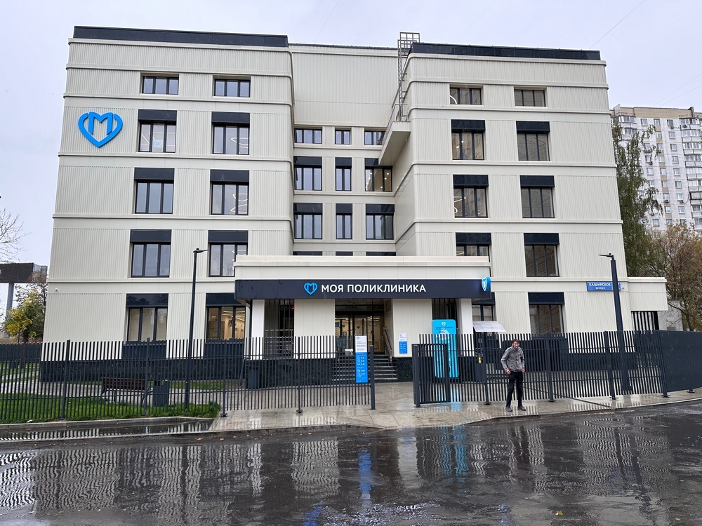 Современное многоэтажное здание поликлиники с серым фасадом и синим логотипом 