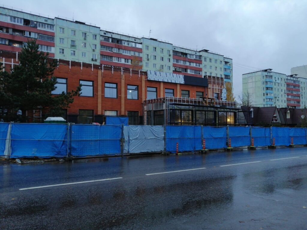 Фотография строительной площадки в городе. Здание в процессе строительства огорожено забором.