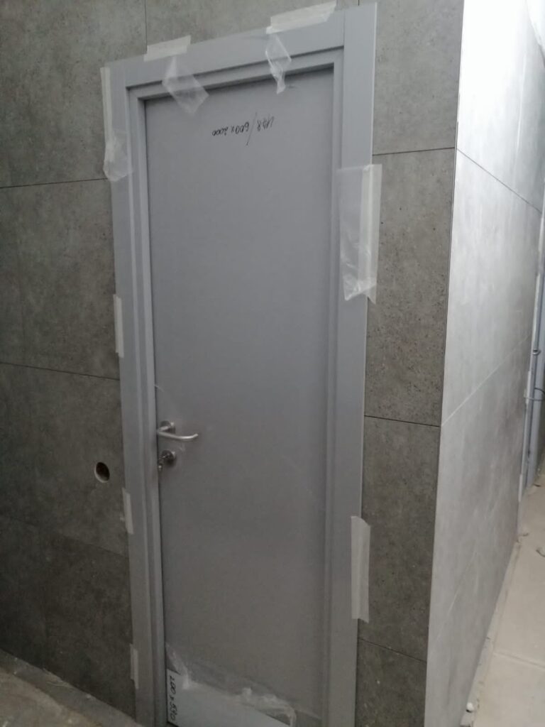 Серая металлическая дверь с ручкой, надпись «148/600x2000», косяк в скотче, серая плитка на стенах.