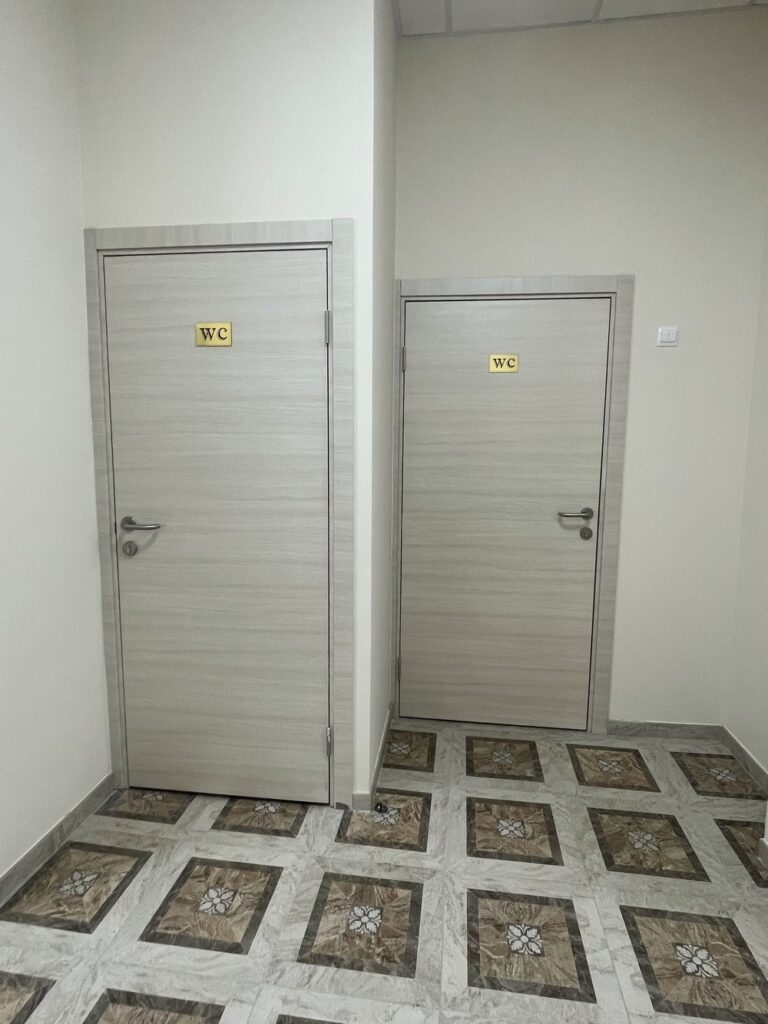 Две светлые двери с табличками «WC», узорчатый плиточный пол, белые стены.