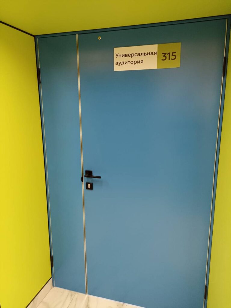 Синяя двустворчатая дверь с табличкой «Универсальная аудитория 315» в ярко-жёлтом проеме, мраморный пол.