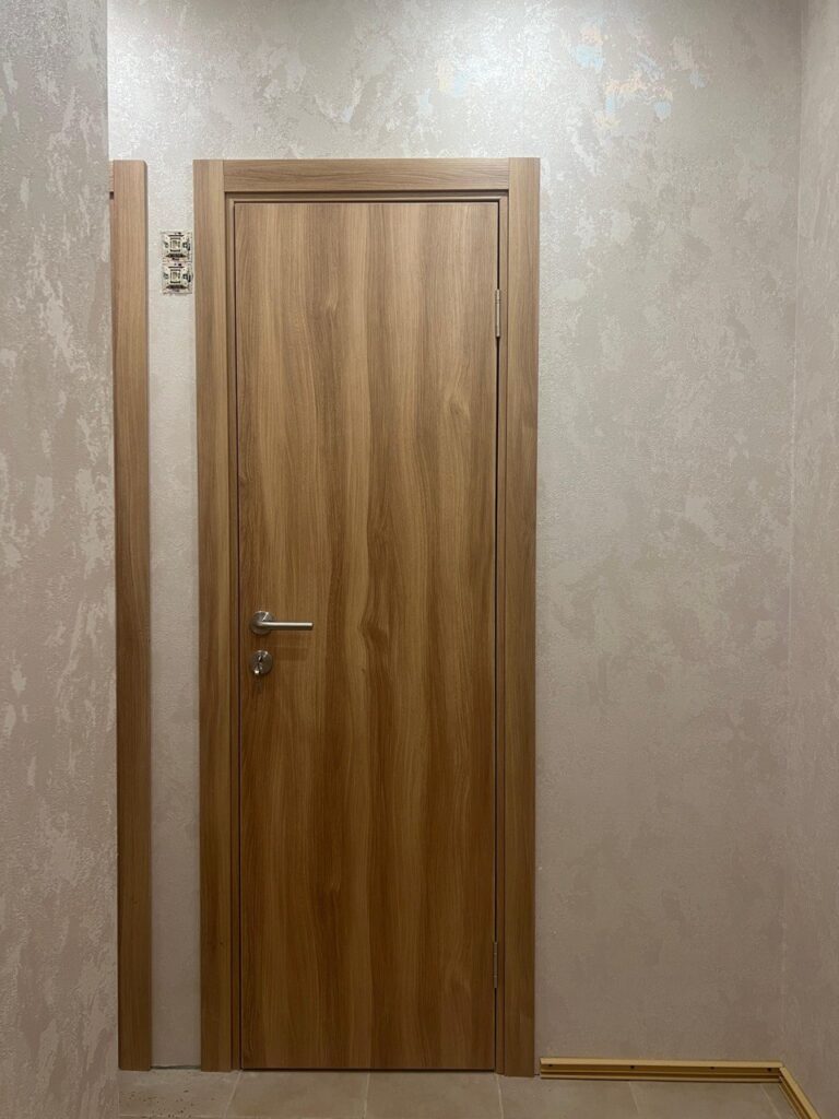 Светлая деревянная дверь с ручкой на фоне фактурной стены